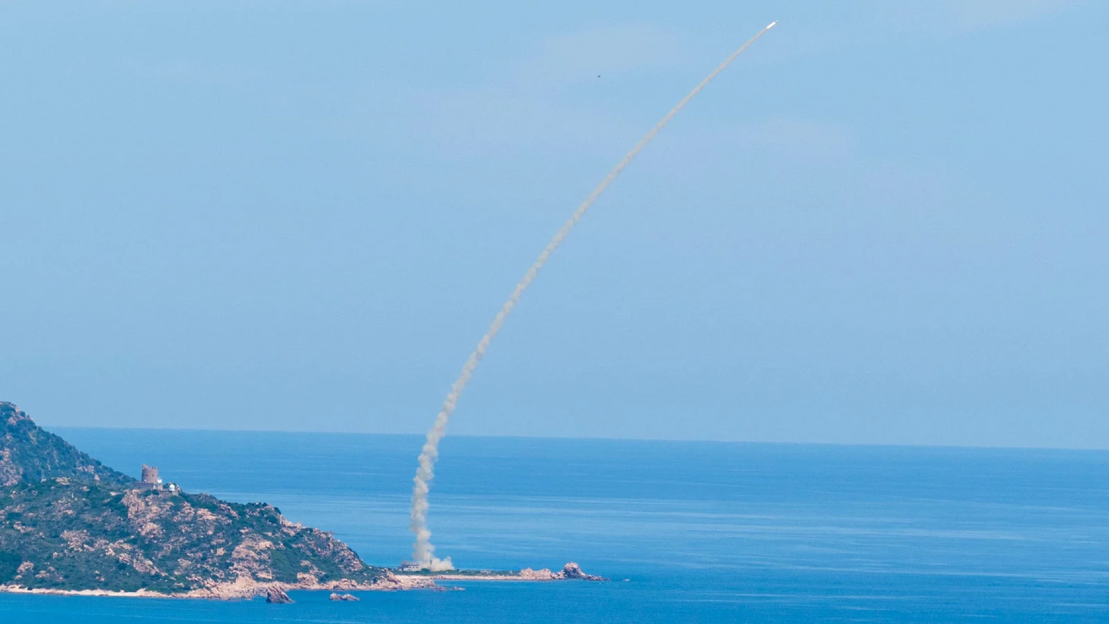 White smoke trail of an Aster 30 missile climbing over the sea after launch from a coastal headland