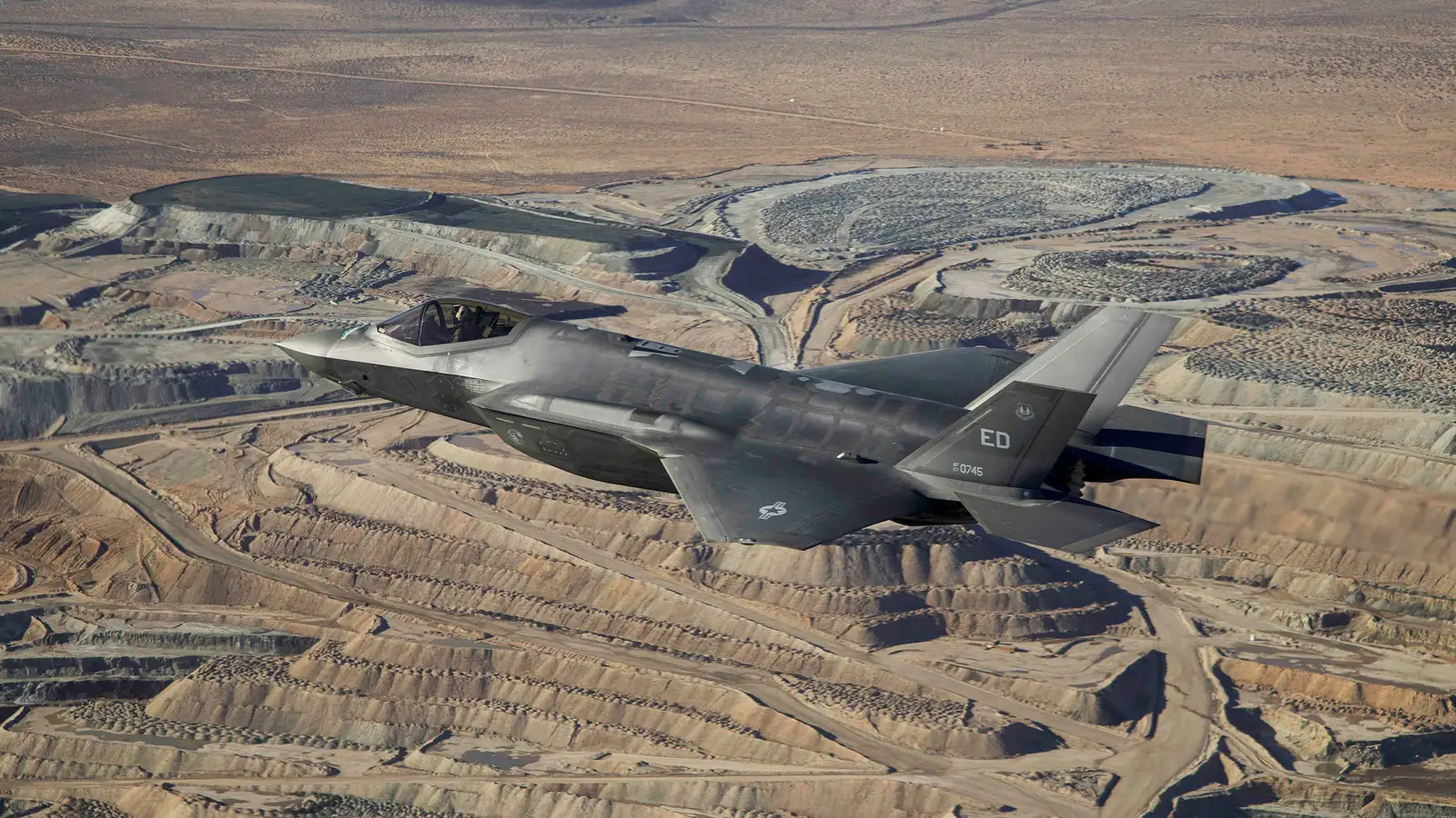 Grey US Air Force F-35A stealth fighter flying low over the brown Mojave Desert during a test flight