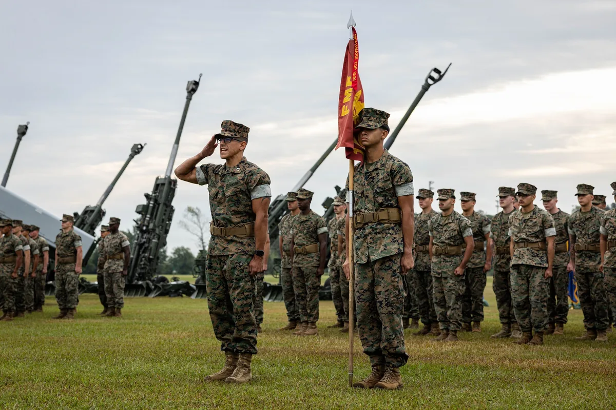 Marines of 1st Battalion, 10th Marines presenting arms in formation on a grass parade field at Camp Lejeune
