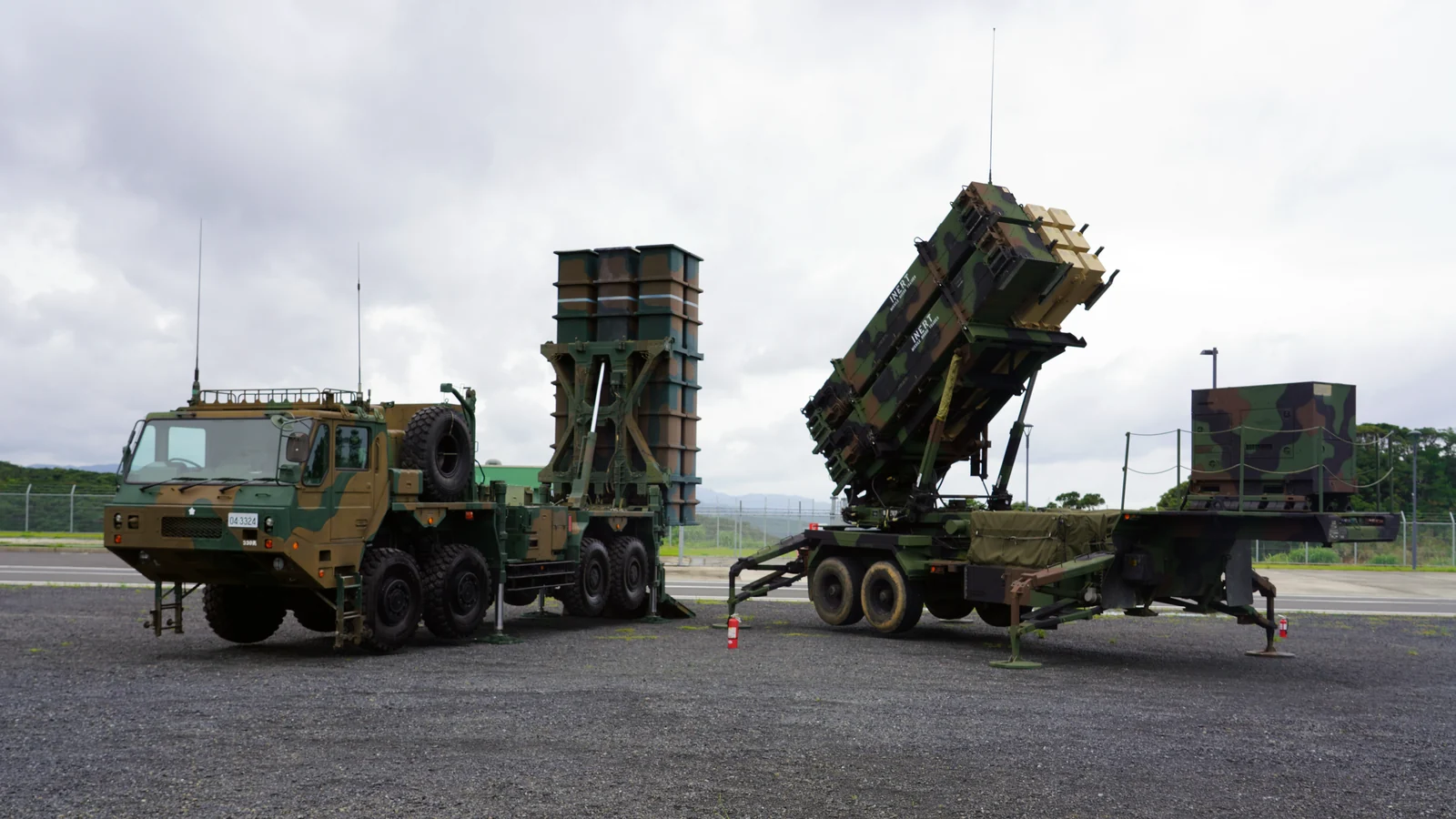 US Army Patriot launcher with its missile canisters raised, parked next to a Japanese air defence vehicle on an airfield