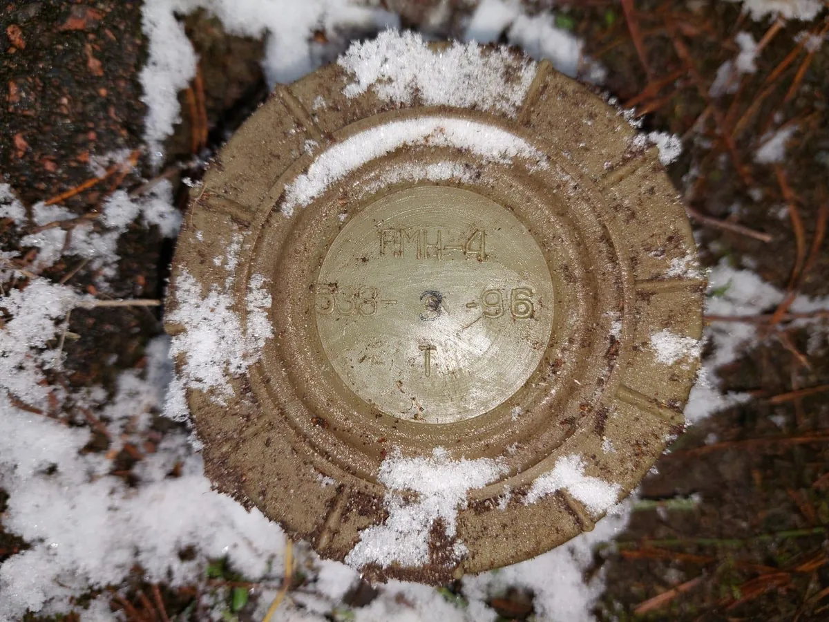A round tan PMN-4 anti-personnel mine marked in Cyrillic lying on ground dusted with snow