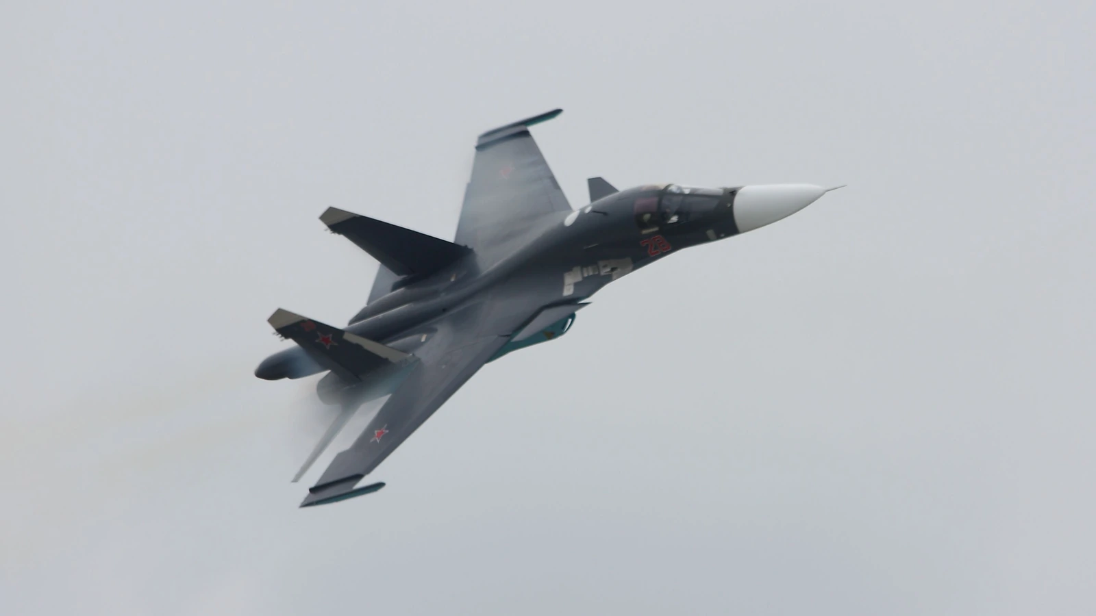 Russian Su-34 fighter-bomber banking hard against an overcast grey sky during a flying display