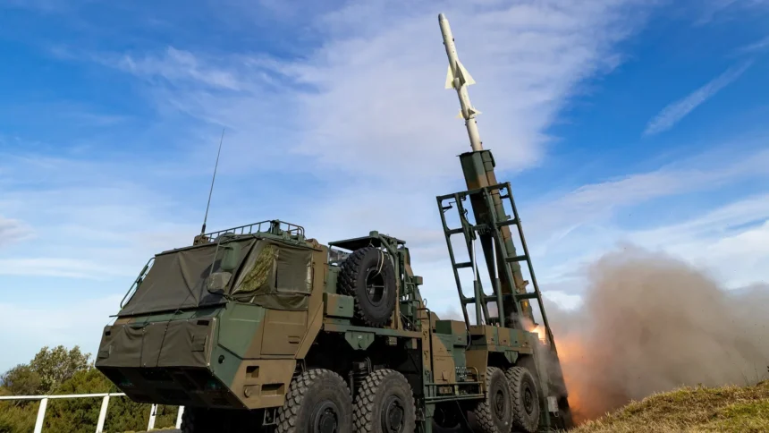 A Japanese Type 12 anti-ship missile leaving its truck-mounted launcher on a grassy range under a blue sky