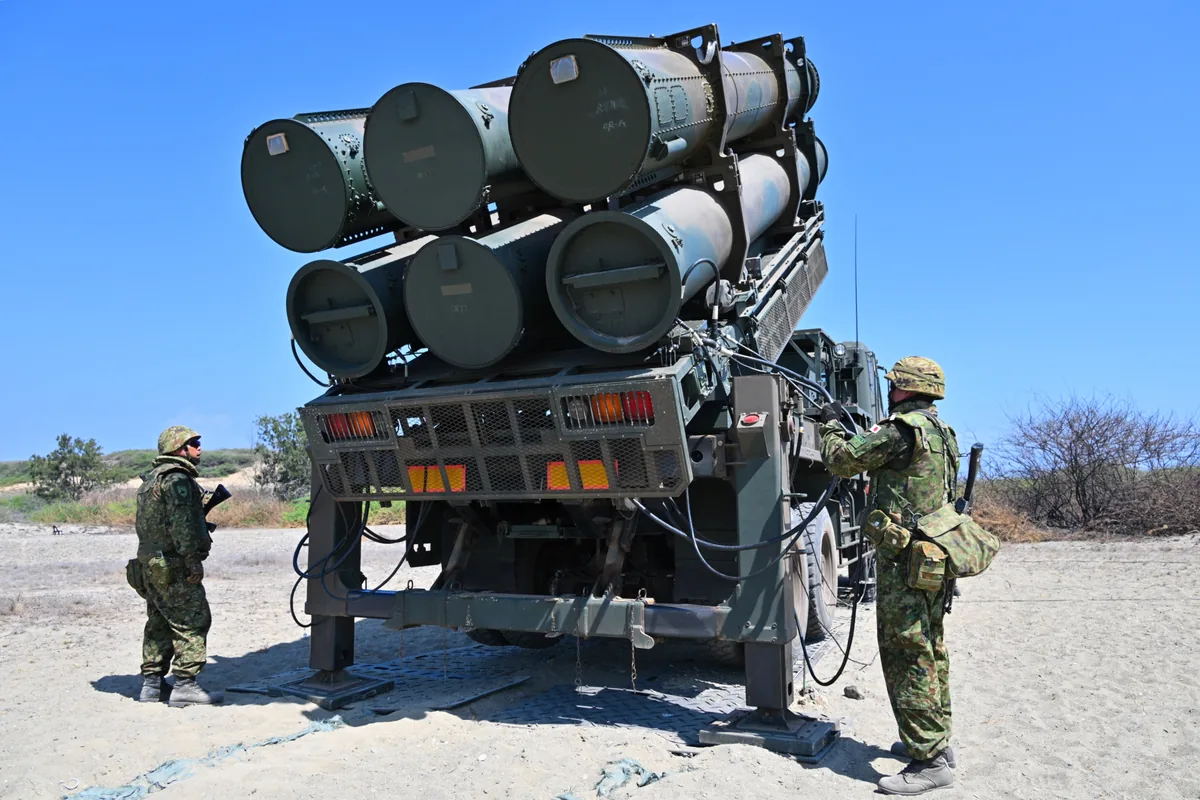 Japanese soldiers beside a Type 88 missile launcher with six canisters raised on a sandy beach range