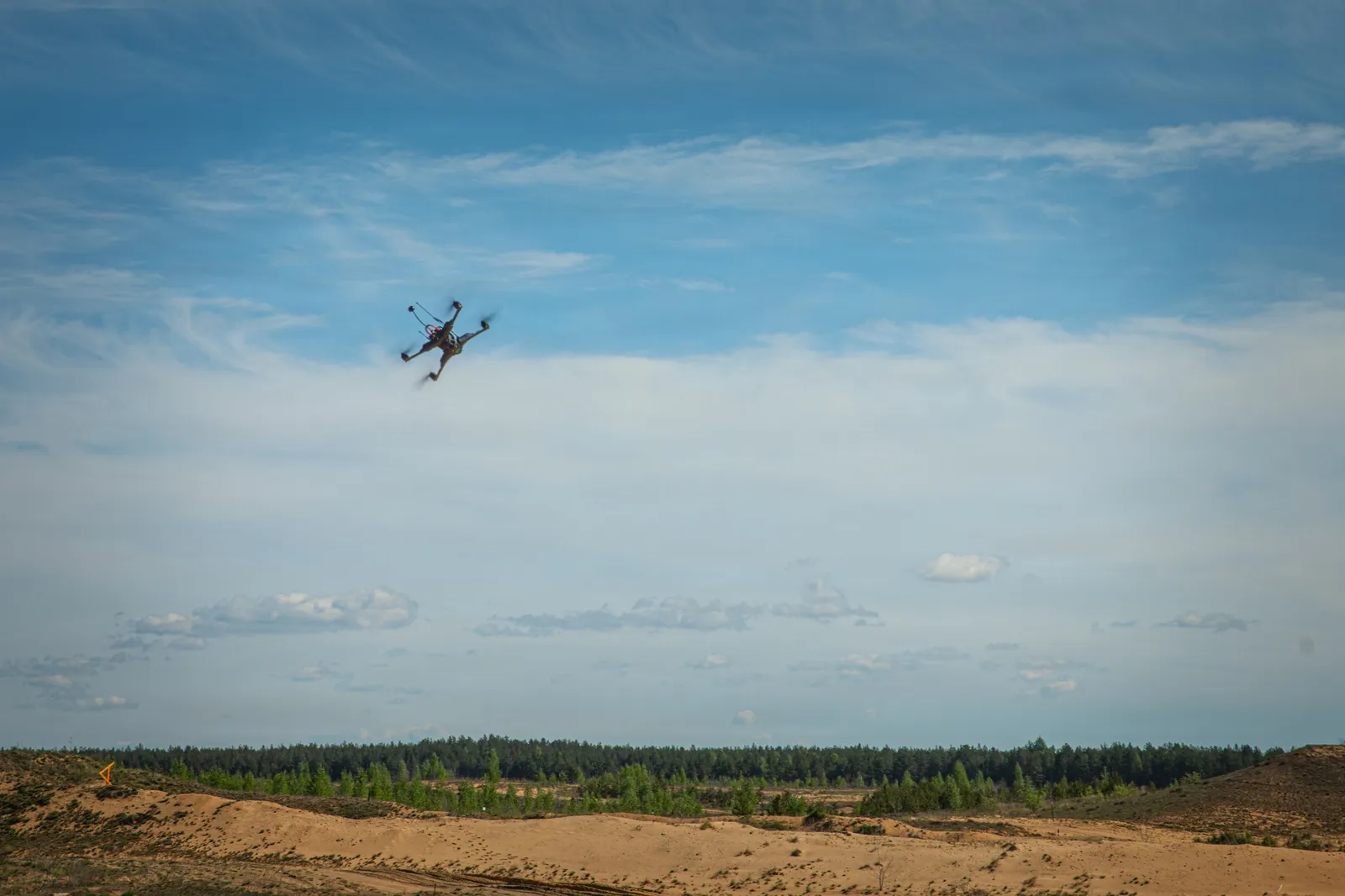 Small quadcopter drone flying over a sandy training area in Lithuania during Project Flytrap