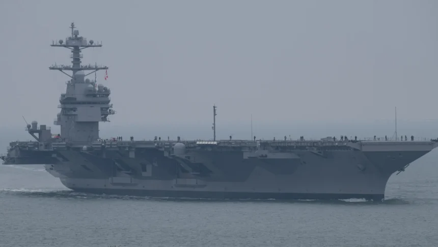 Grey US Navy aircraft carrier John F. Kennedy sailing in hazy weather with crew lining the flight deck